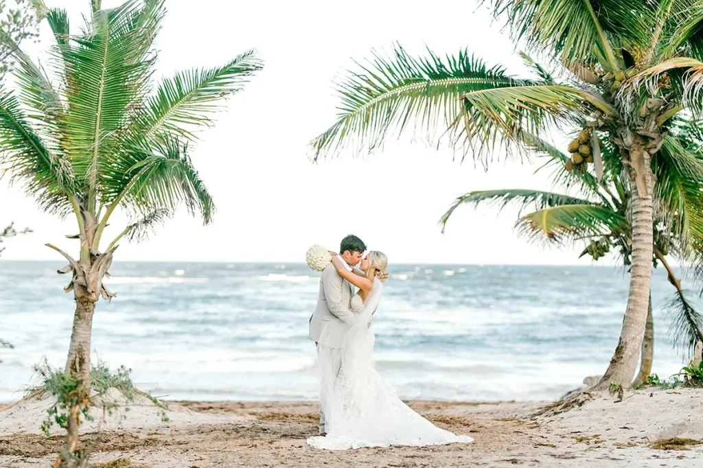 Newlywed couple sharing a kiss on the beach at UNICO 2087 in their wedding garments
