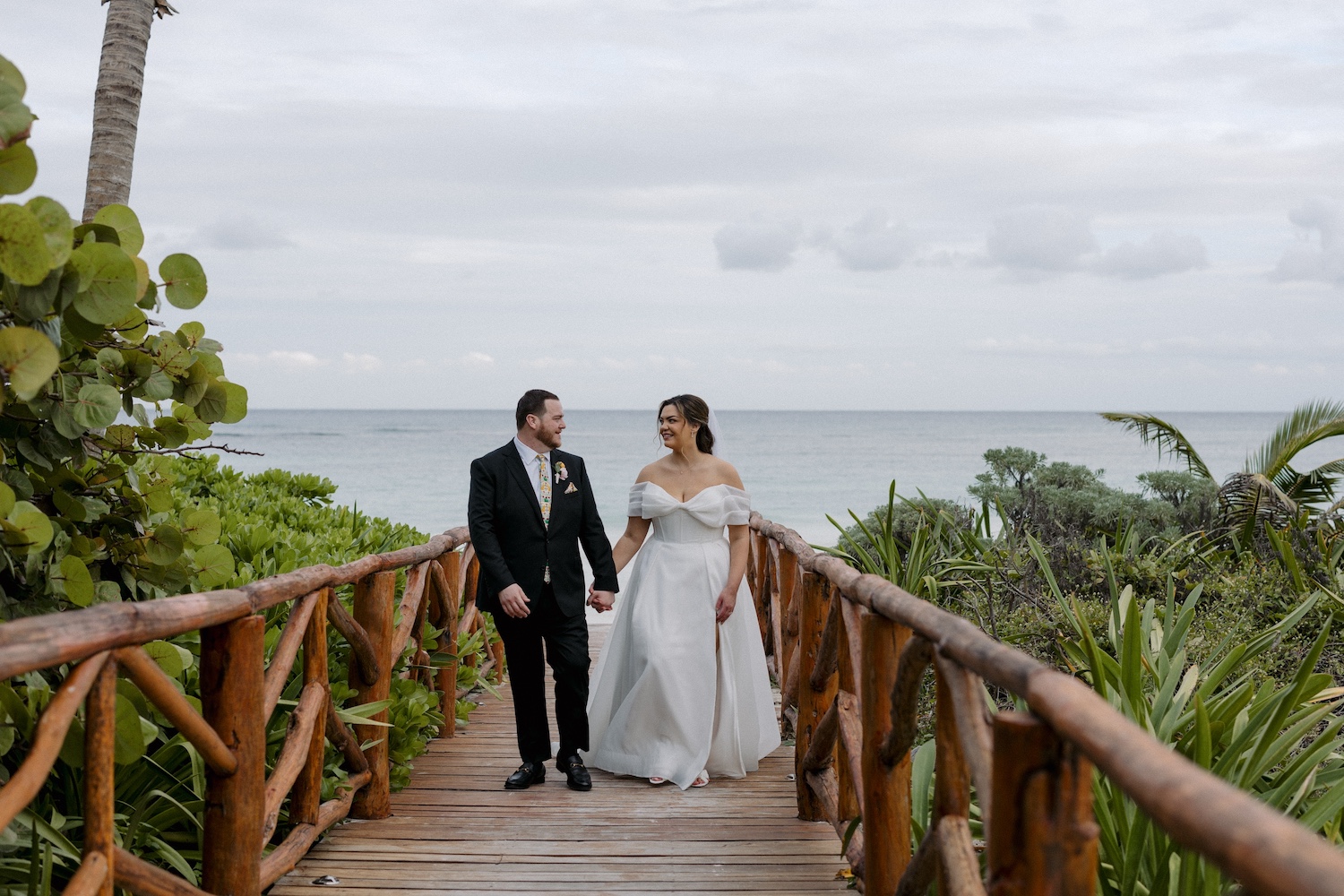 Bride and Groom walking down wooden boardwalk with ocean in background.
